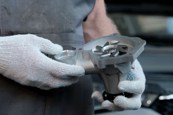 An auto mechanic holds a new water pump in his hands for a repair