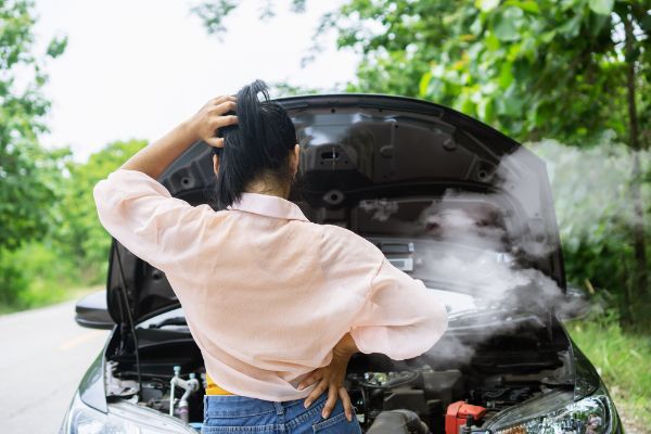 woman having problem with broken, overheat car while driving alone on the road standing with smoke